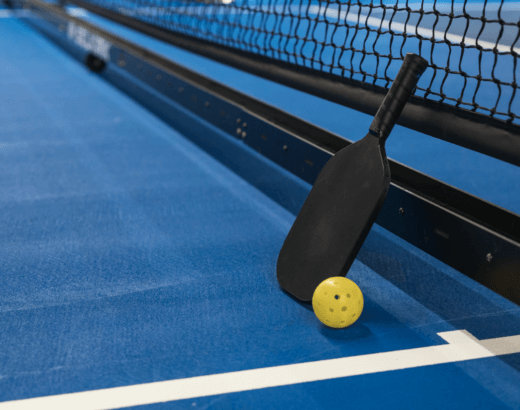 pickleball paddle and ball resting against a pickleball net.